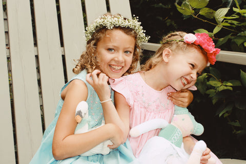 two laughing girls wearing pink and blue smocked dresses with flower crowns