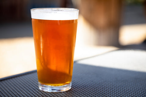 A glass of beer sits on a table in the sun.
