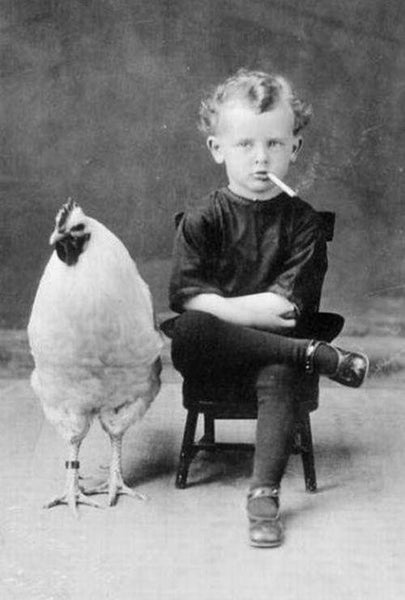 Photo of young child smoking cigarette next to a chicken