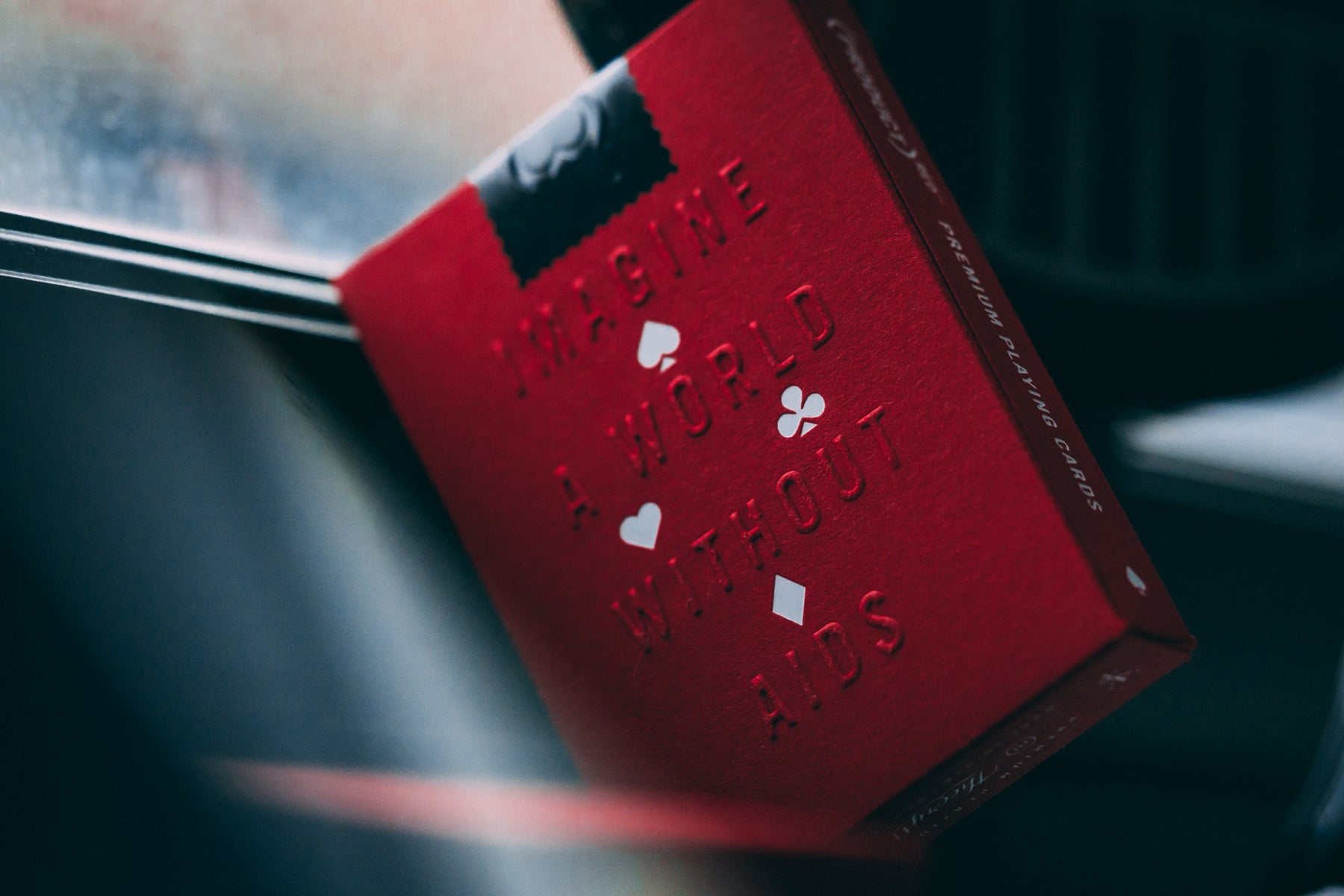Close up photograph of a red deck of playing cards that were custom designed by Theory11. The deck is embossed with the words Imagine A World Without Aids. 