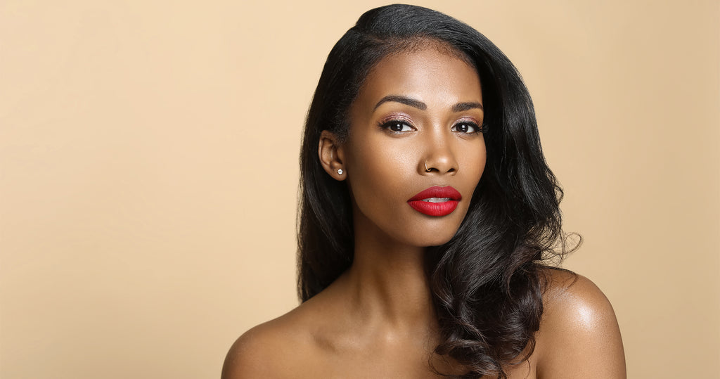 Portrait of The Lip Bar founder Melissa Butler, looking directly at the camera with bare shoulders, against a beige background with bright red lipstick on and hair pulled to the side, over her shoulder.