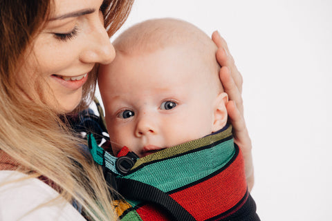 close up of white woman carrying white baby in a Carousel of Colors Mesh Lenny Upgrade fully adjustable soft structured carrier from Lenny Lamb. The front panel is black mesh and the carrier itself is bold stripes of color with thin black stripes demarcating the colors
