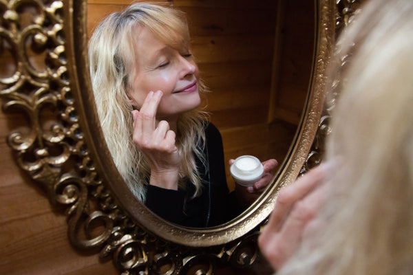 woman applying moisturizer in the mirror