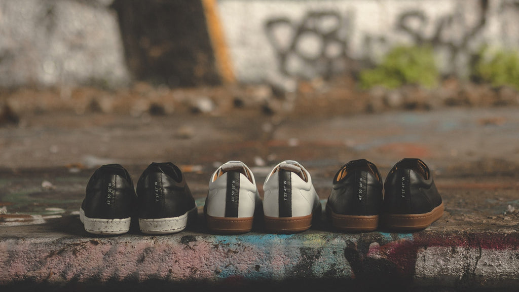 Trois paires de chaussures oth-paris de couleurs différentes avec des semelles en pneu recyclé sur un trottoir tagué