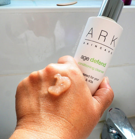 Models hand with ARK Skincare Age Defend Cleanser formula on hand and holding cleanser bottle 