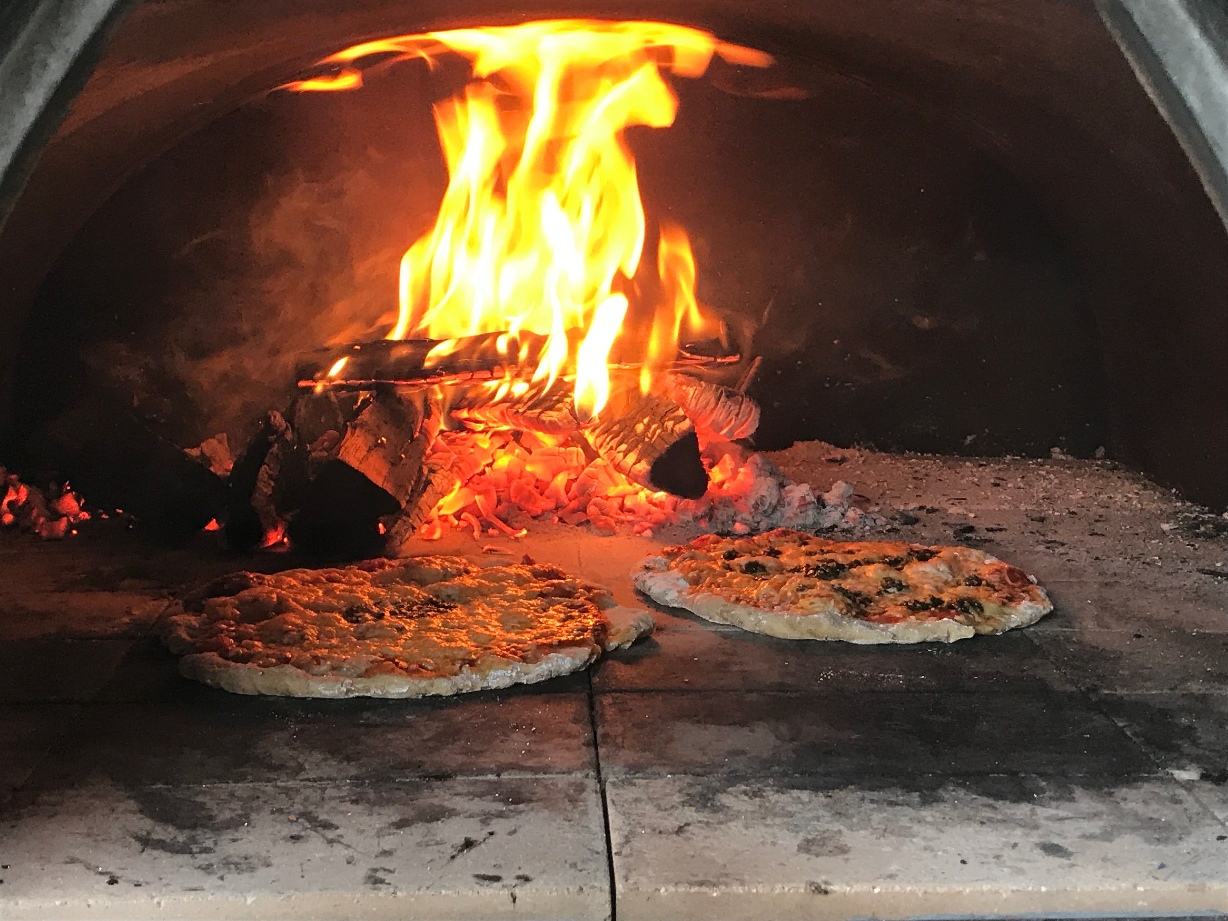 Two pizzas cooking in a large wood burning pizza oven