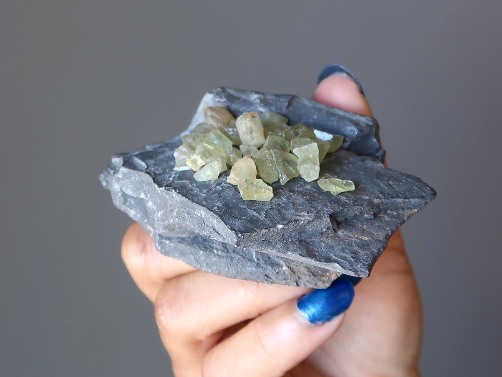 hand holding green apatite gemstones on gray fossil rock at satin crystals