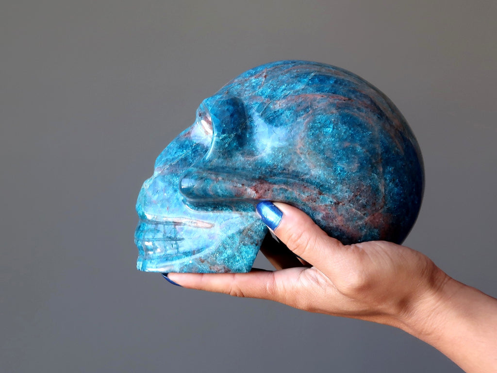 hand holding a big blue apatite gemstone skull carving at satin crystals