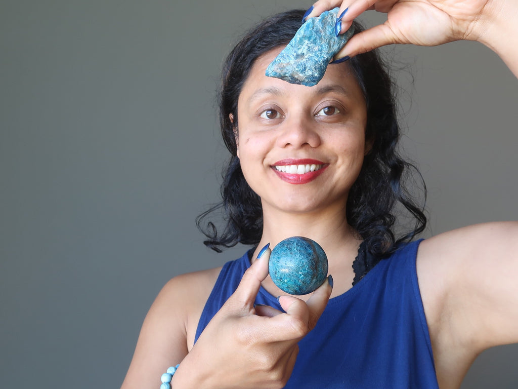 sheila of satin crystals holding a raw blue apatite rock and polished sphere over her chakras for healing