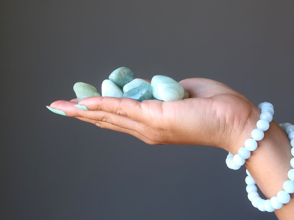 hand wearing aquamarine stretch bracelets holding a pile of aquamarine tumbled stones