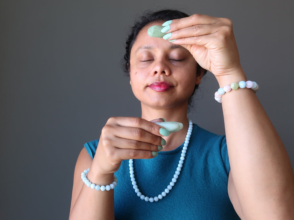 sheila of satin crystals holding up aquamarine tumbled stones over her third eye and throat chakras