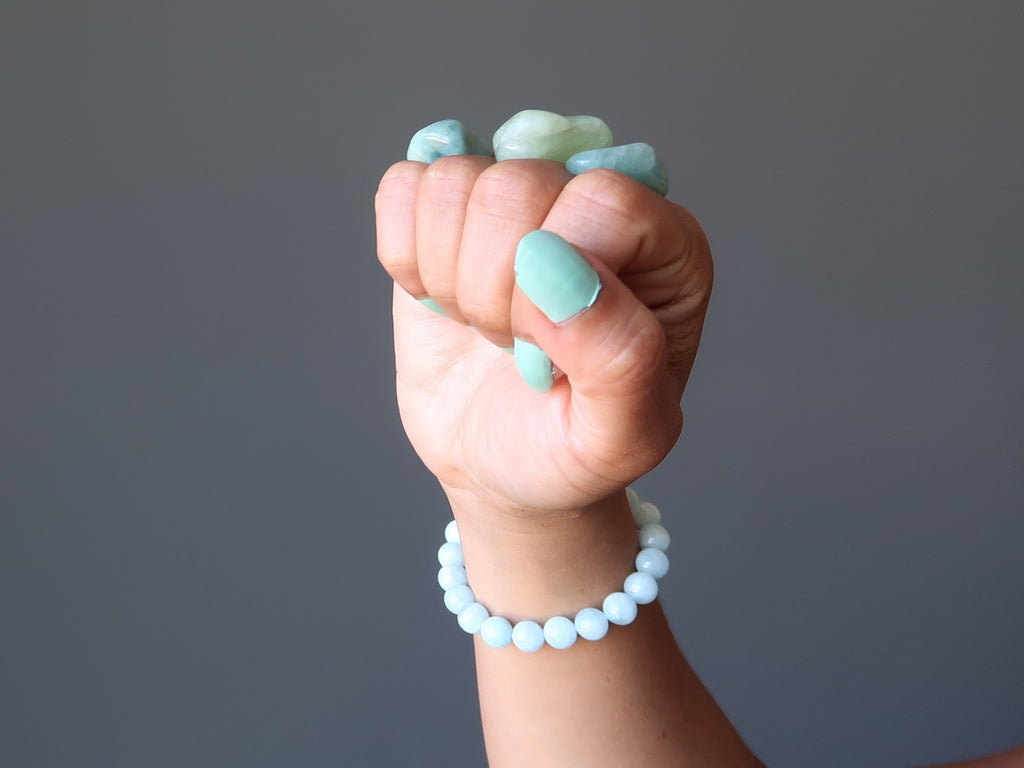 hand making a fist wearing aquamarine stretch bracelet and balancing aquamarine tumbled stones