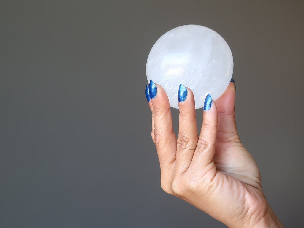 sheila of satin crystals' hand holding up a white calcite sphere