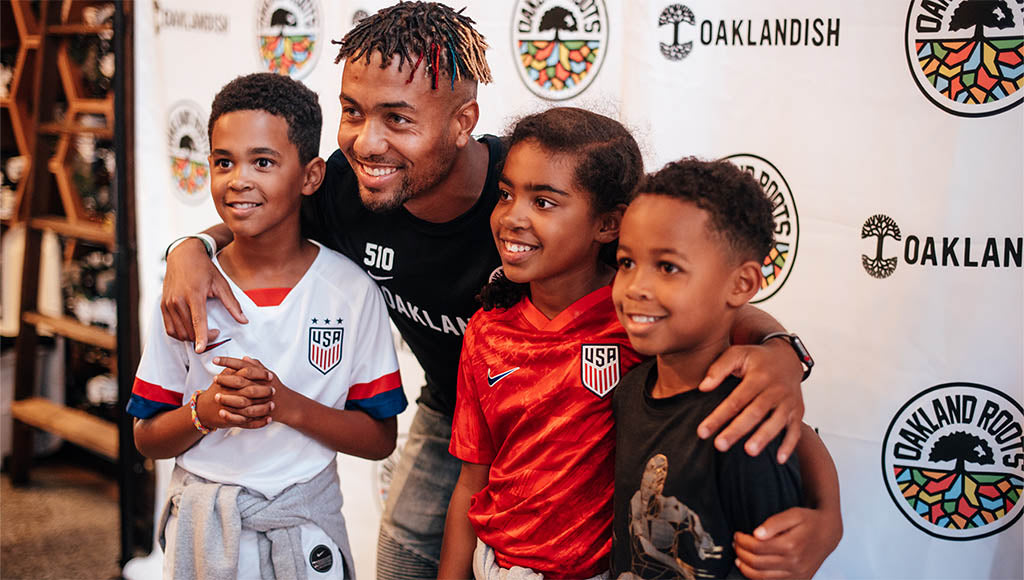 Oakland Roots player posing with some kids.