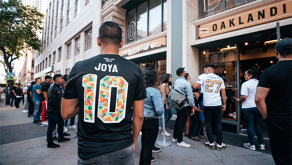 Crowd in front of store, back view of guy wearing custom JOYA jersey.