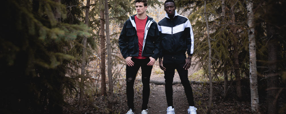 Shop Kuwallatee; two men wearing Kuwallatee jackets, jeans, and tees standing in wooded area