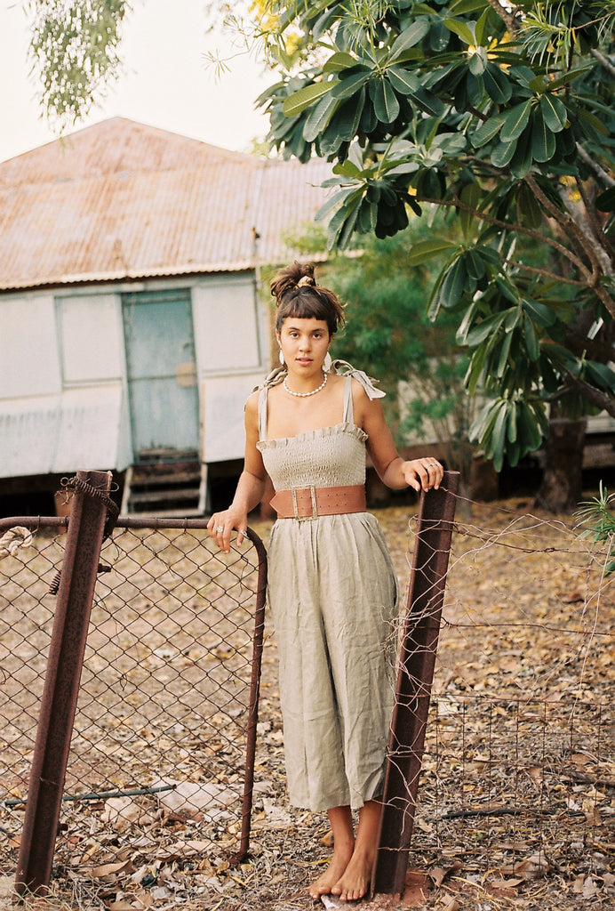 Model Broome, taking a pose on a rusty fence with her jumpsuit and brown belt