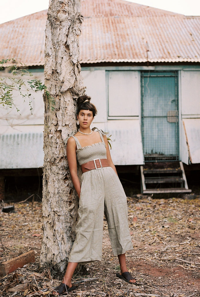 our model, wearing a jumpsuit and a waist belt, leaning on a tree